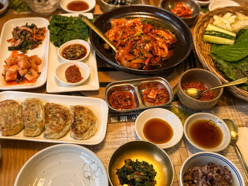Table spread with stir-fried kimchi, pan-fried jeon, lettuce wraps and banchan
