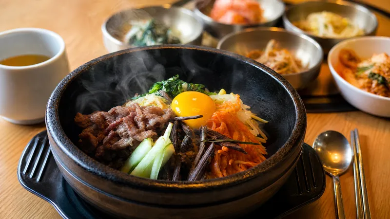 Bibimbap steaming in a hot stone bowl, topped with a raw egg yolk