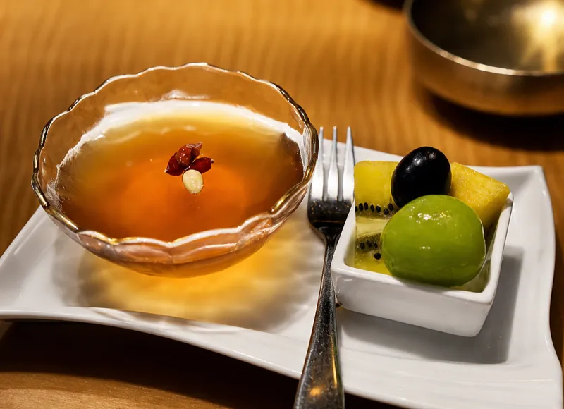 Chilled Korean punch garnished with a goji berry, served with a plate of fresh fruit