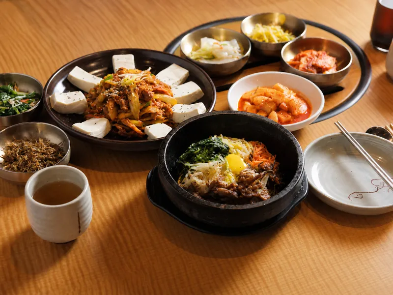 Dubu kimchi with stone-bowl bibimbap and banchan set across a wooden table