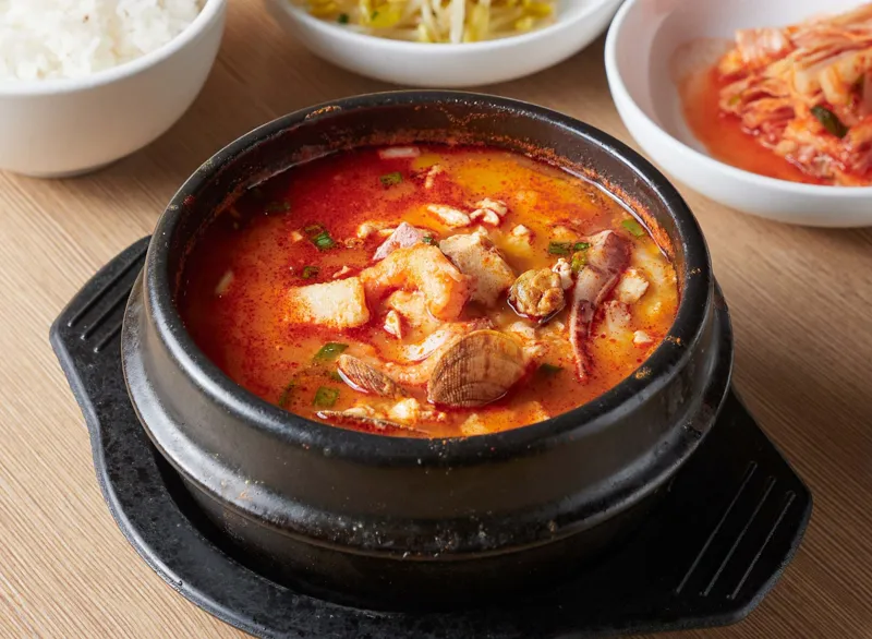 Kimchi stew bubbling in a black stone pot, served with rice and kimchi